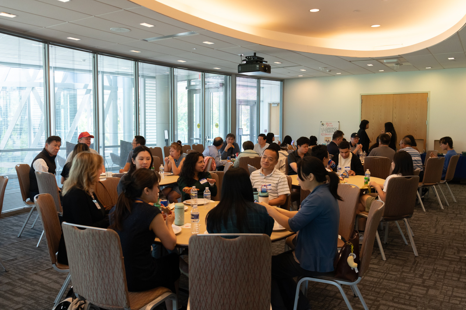 Attendees network over refreshments at round tables in a sunlit room.