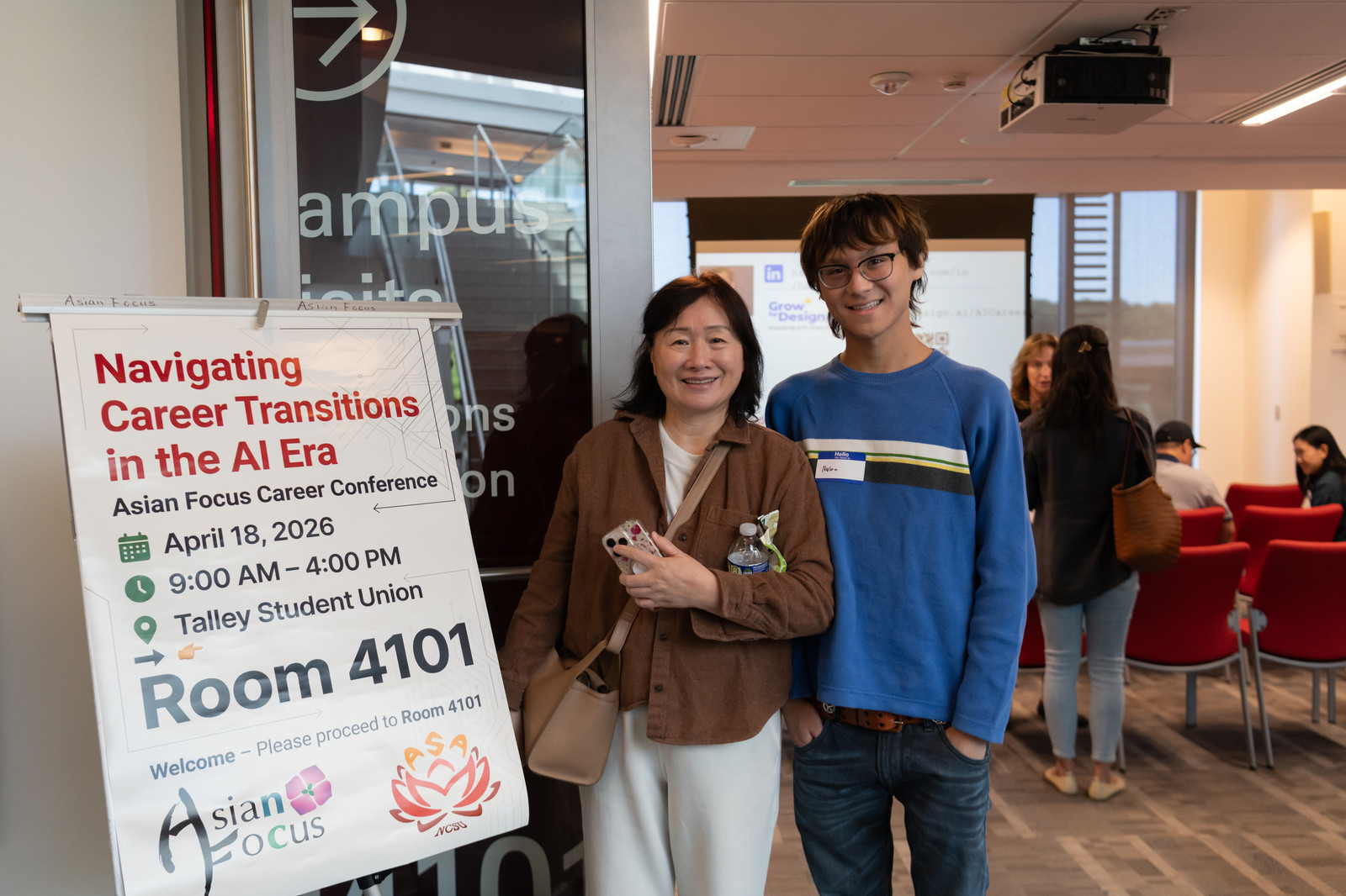 Two attendees smile beside the conference welcome sign for Navigating Career Transitions in the AI Era at Talley Student Union, Room 4101.