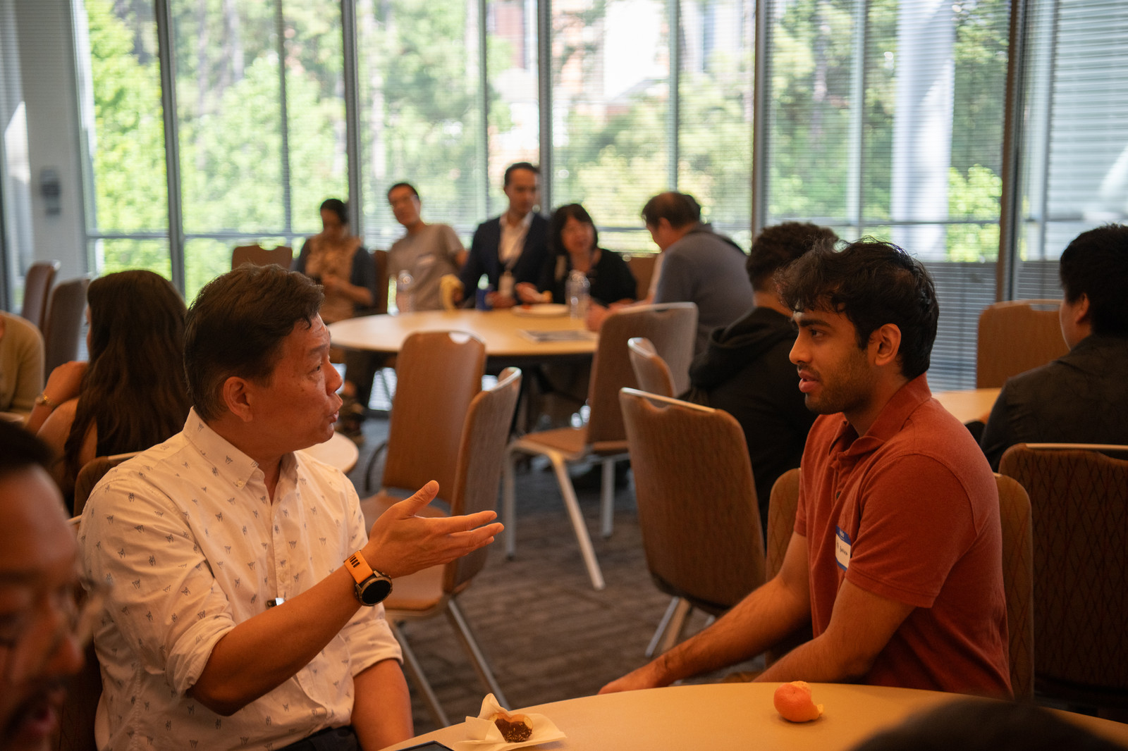 Two attendees in animated conversation at a round table during a networking break.