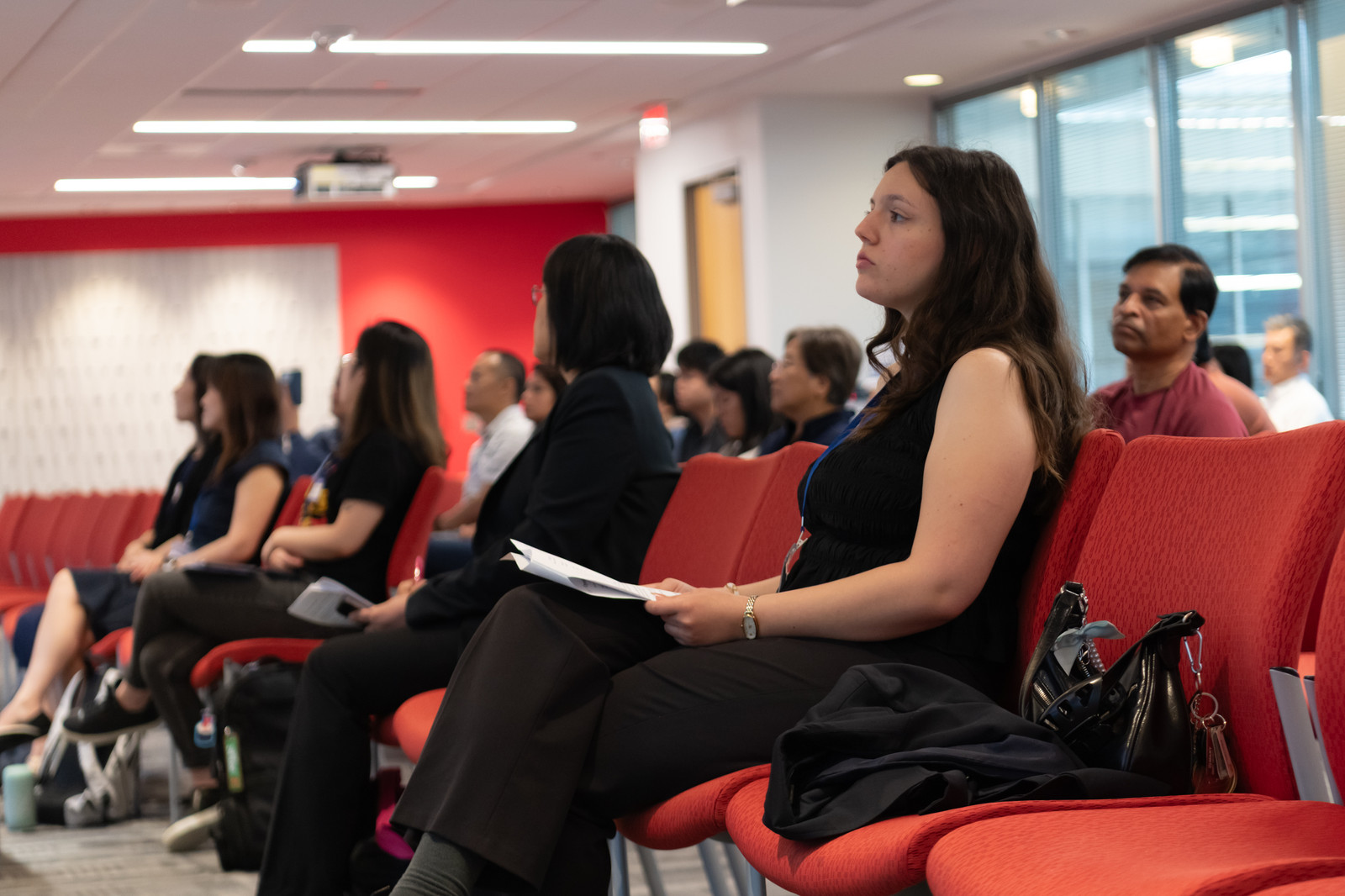 Attendees listen attentively from the red seating in the conference room.