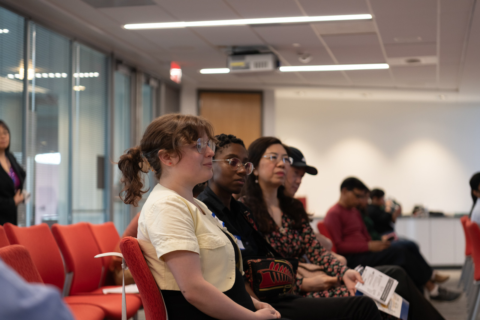 Attendees seated and listening, a participant in a yellow blouse in the foreground.