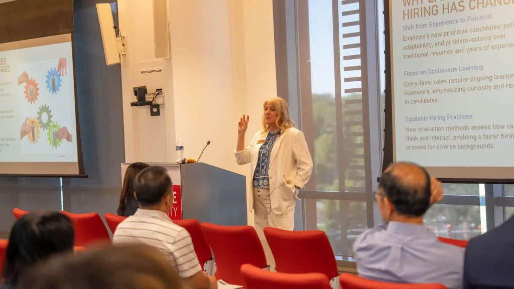 A speaker in a cream blazer presents 'Why Early-Career Hiring Has Changed.'