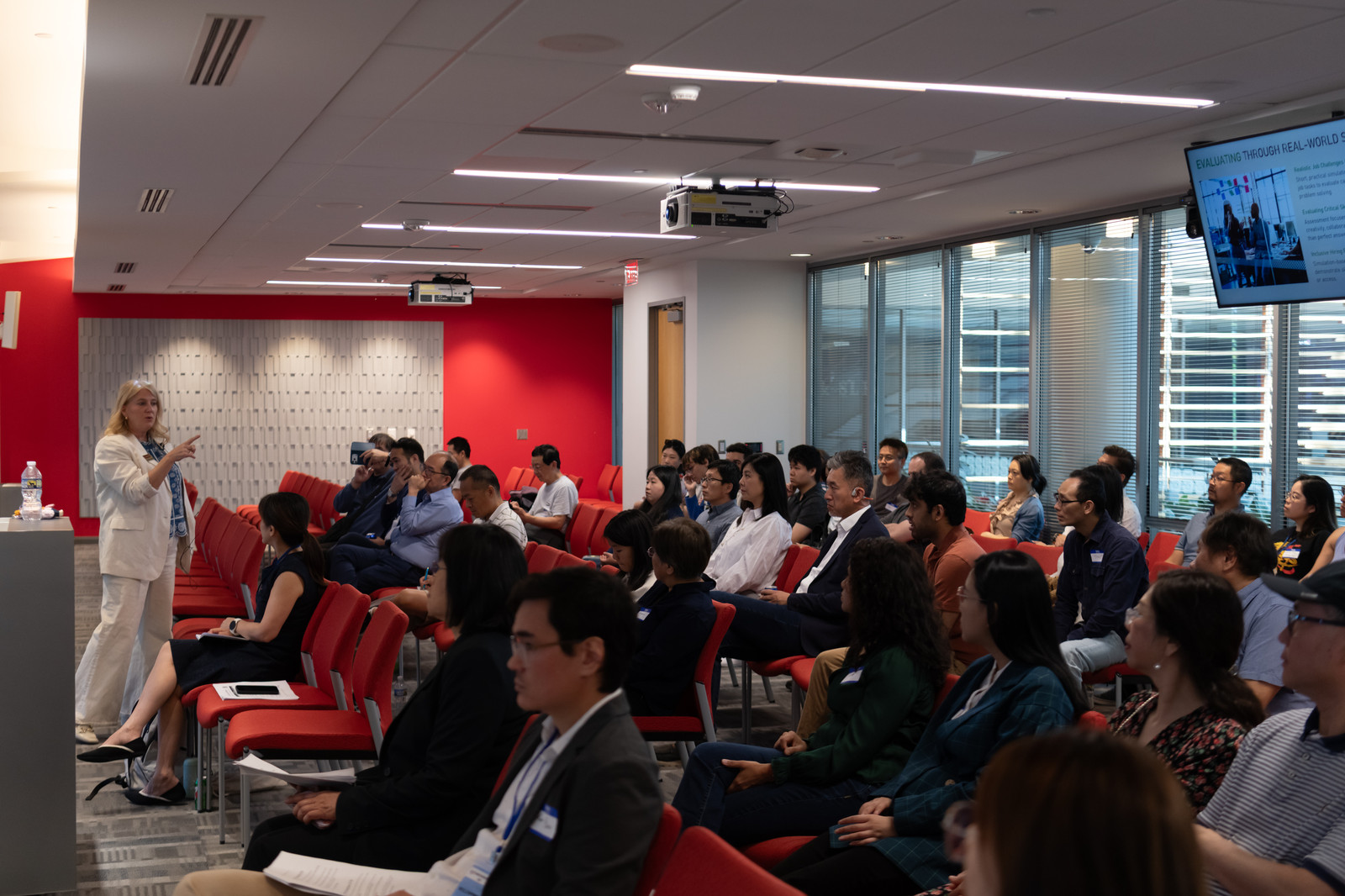 A wide view of a speaker addressing a full room of seated attendees.