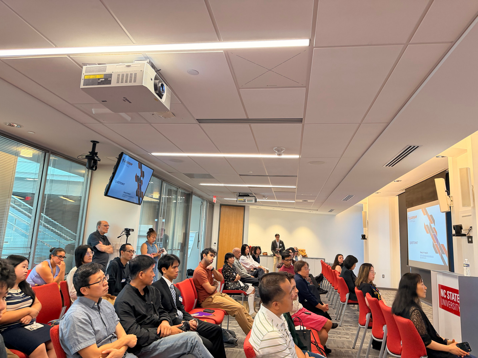 A wide view of the conference room as attendees watch a presentation.