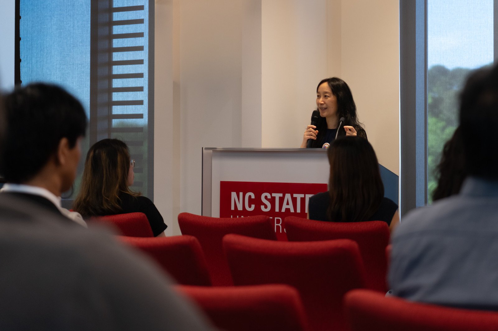 An organizer welcomes the room from the NC State podium to open the day.