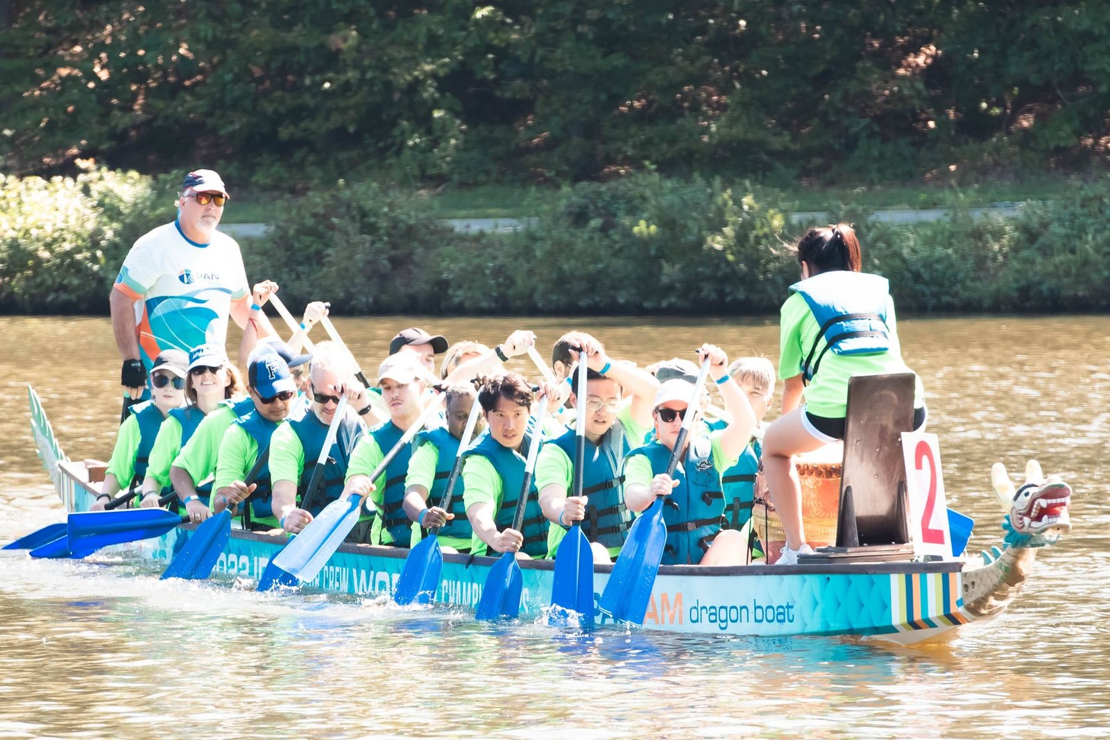 A dragon boat team in teal life vests paddling in unison during an Asia Fest race