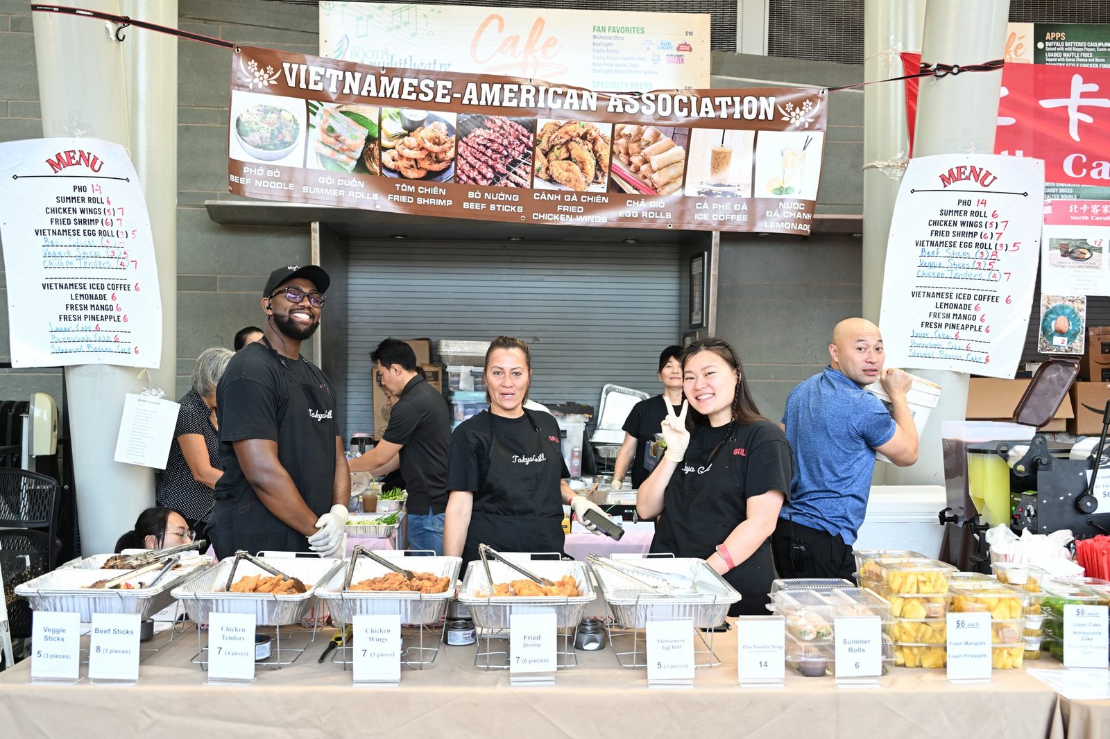 Smiling volunteers serving Vietnamese-American cuisine at a festival food booth