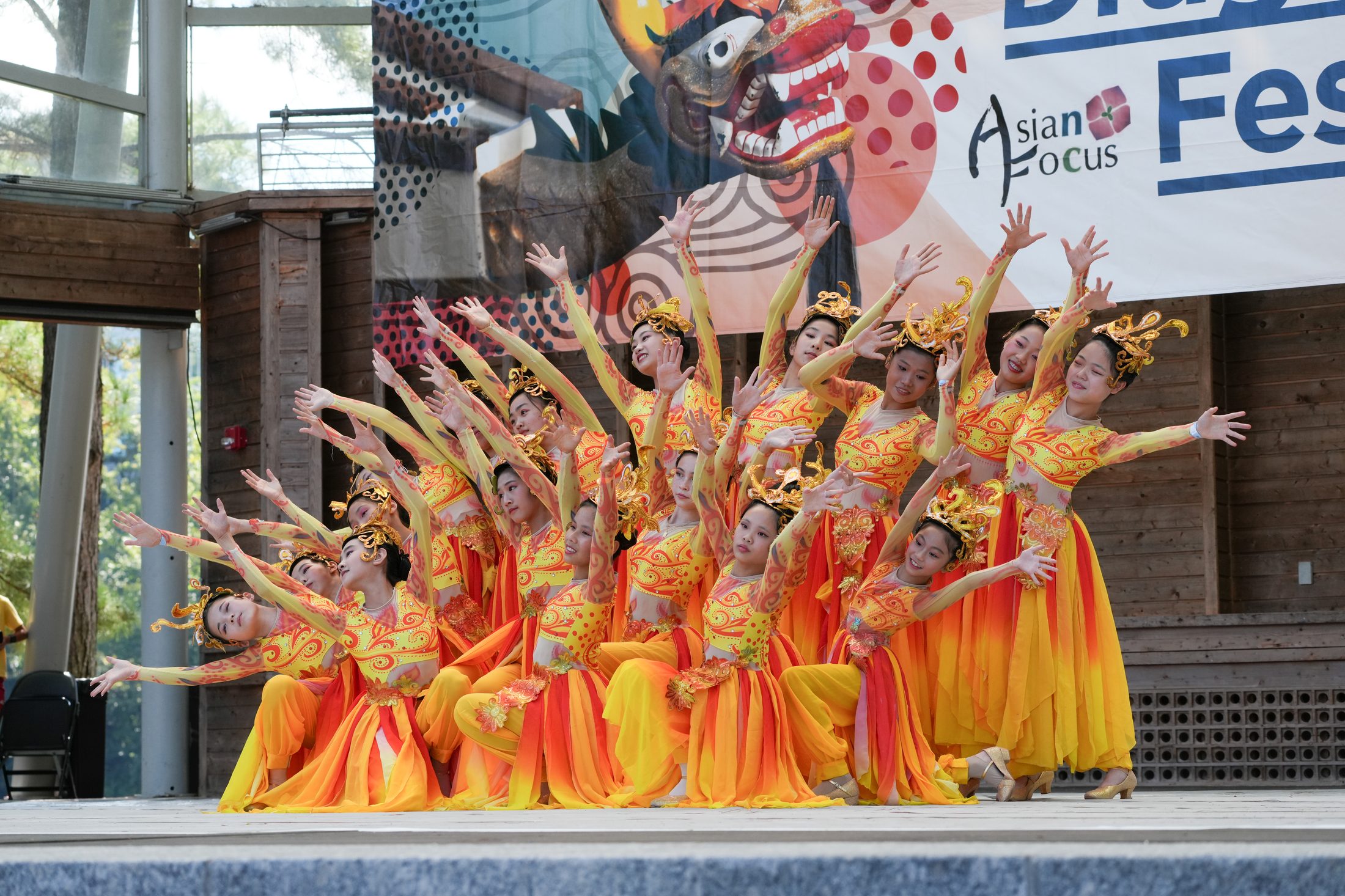 Dozens of dancers in flowing orange and gold costumes performing on stage at Asia Fest