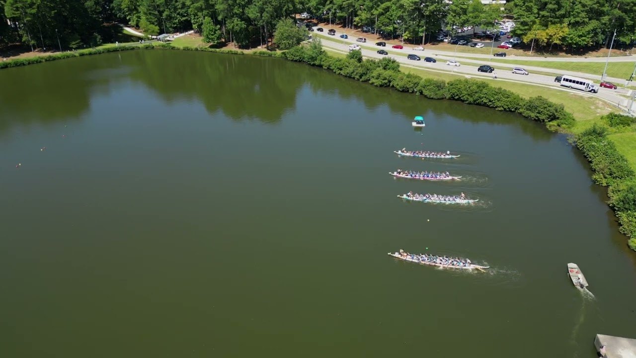 Aerial view of four dragon boats racing across Symphony Lake at Koka Booth Amphitheatre during Asia Fest